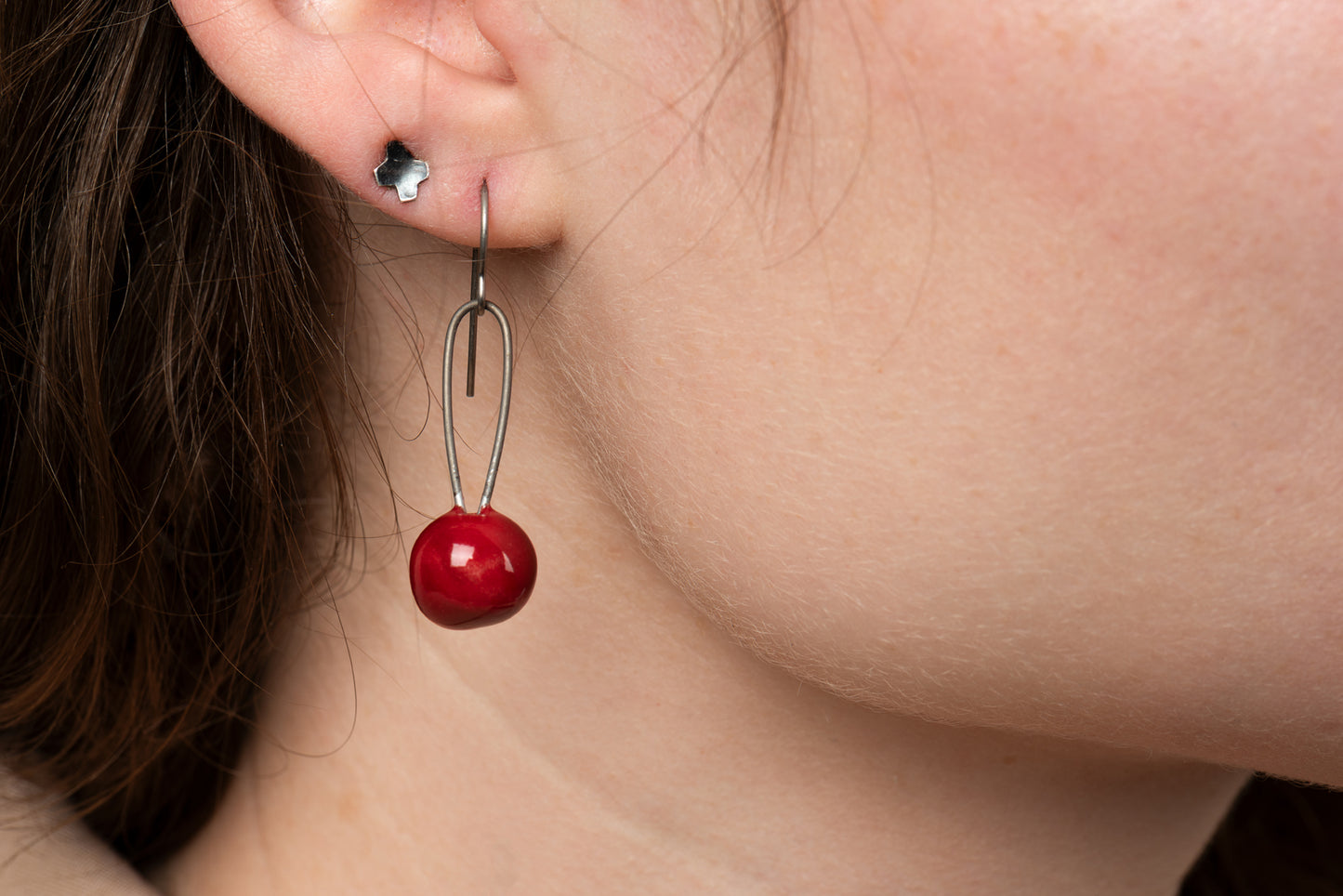 A closeup of one of Joy Tanner's red sphere ceramic earrings hanging in someone's ear.