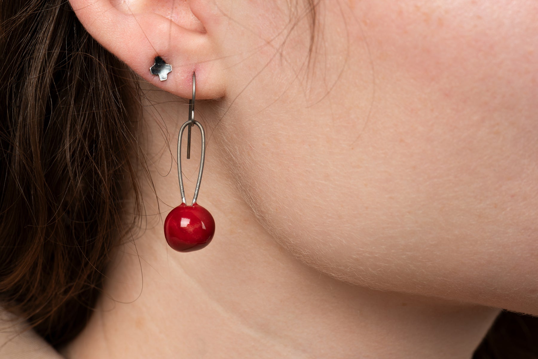 A closeup of one of Joy Tanner's red sphere ceramic earrings hanging in someone's ear.