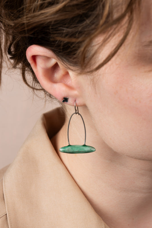 A closeup of one of Joy Tanner's green ceramic and wire earrings hanging in someone's ear. Image by Loam.