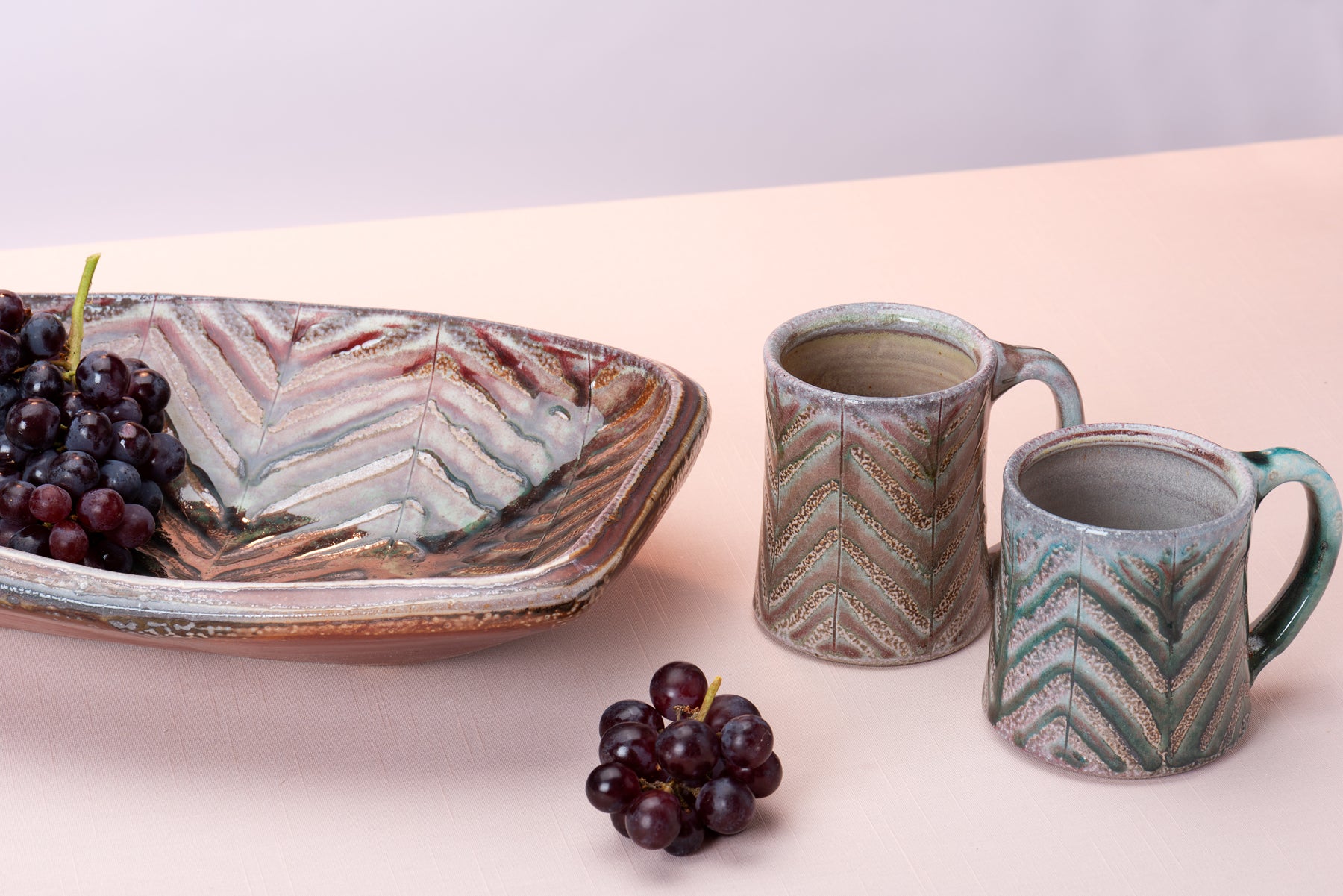 A couple pieces of handmade pottery by artist Joy Tanner sit on a peach table against a blush-purple  backdrop. Image by Loam