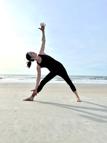 Person practicing yoga on a sandy beach with ocean and sky in the background