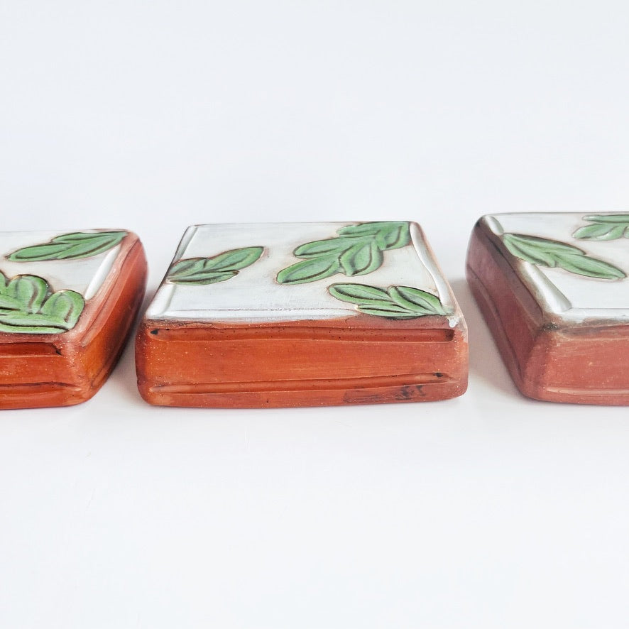 This square wall tile is made from red earthenware clay. The hand carved green leaf pattern contrasts nicely with the white surface and the red clay. Simply display on your wall alone, or in a grouping.