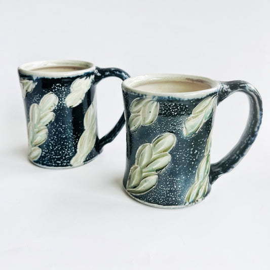 handmade black pottery mug with white and green leaf accents