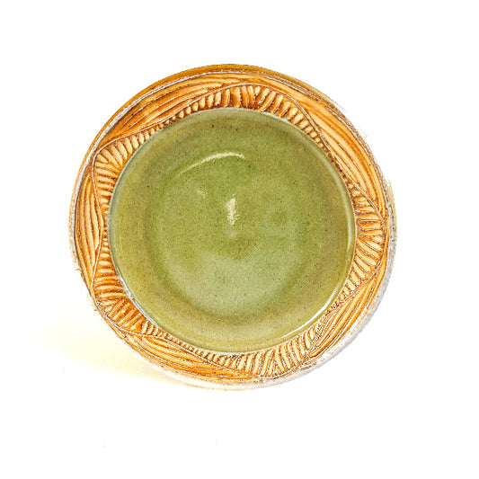 A handmade plate makes your food taste better. This plate is wheel thrown from stoneware clay. The leaf pattern that is hand carved is inspired by nature. The rim is yellow and the interior of the plate is light green.