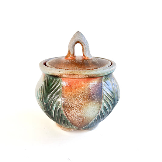 This small round handmade jar could be used to store tea bags, sugar, or candy. The green leaf pattern that is hand carved is inspired by nature.
