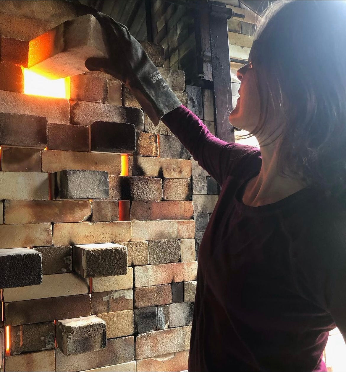 Potter Joy Tanner removing a red hot bring from a wall of her actively firing kiln