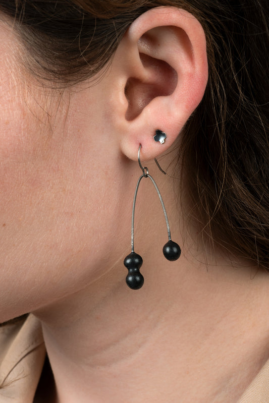 A closeup of one of Joy Tanner's black dangle ceramic earrings hanging in someone's ear.