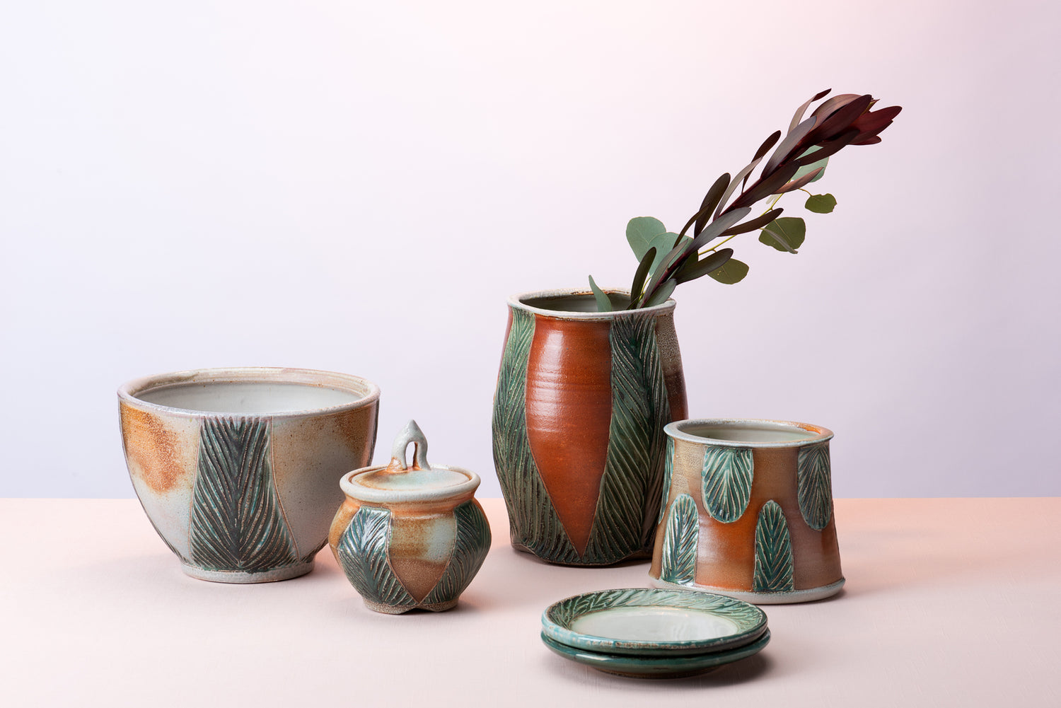 A group of handmade pottery pieces by artist Joy Tanner sit on a peach table against a blush-purple  backdrop. Image by Loam 