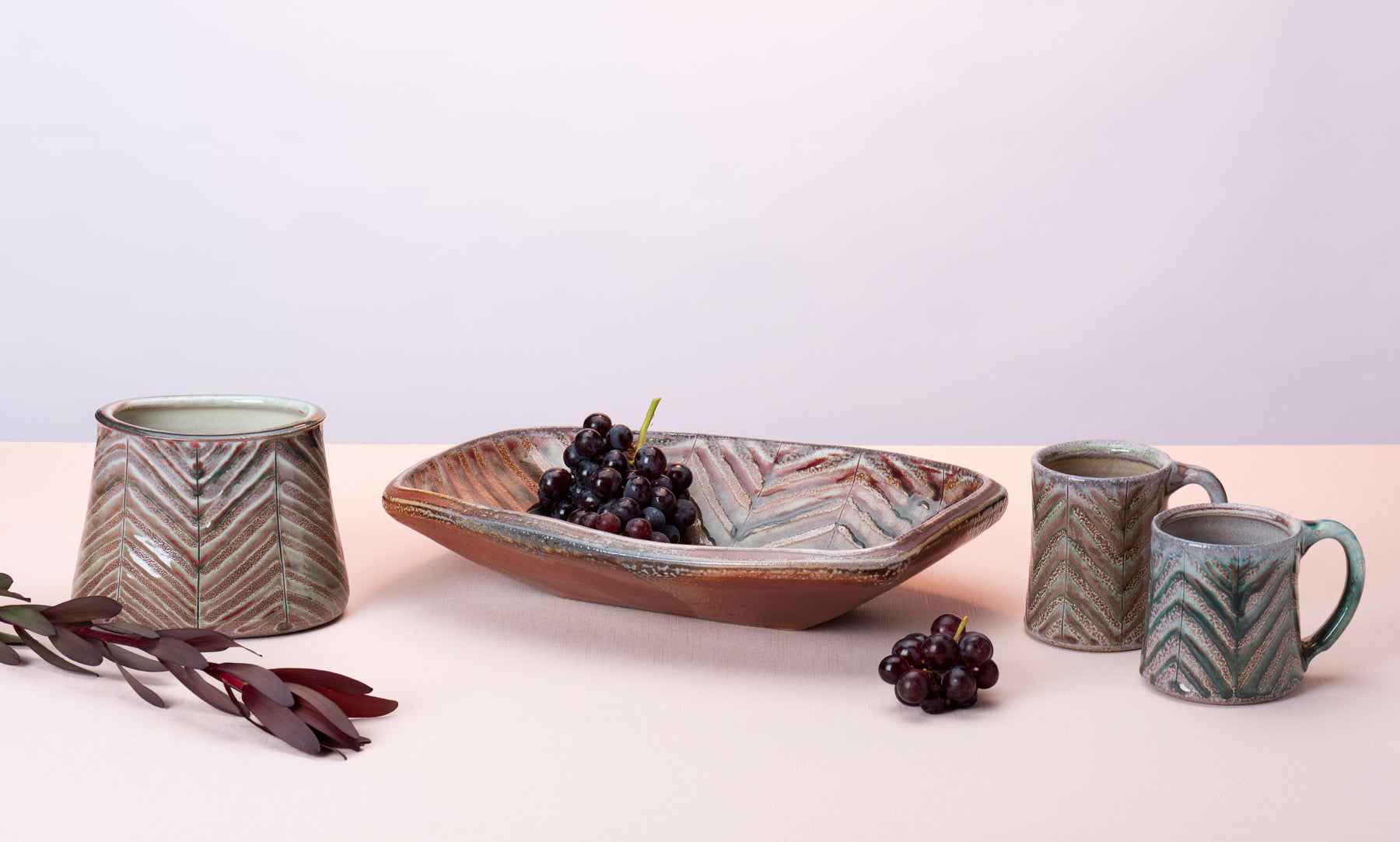 Several pieces of handmade pottery by artist Joy Tanner sit on a peach table against a blush-purple  backdrop. Image by Loam 