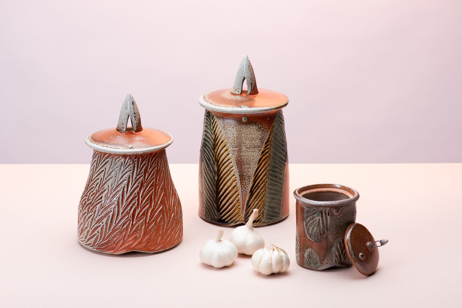 A couple pieces of handmade pottery by artist Joy Tanner sit on a peach table against a blush-purple  backdrop. Image by Loam 