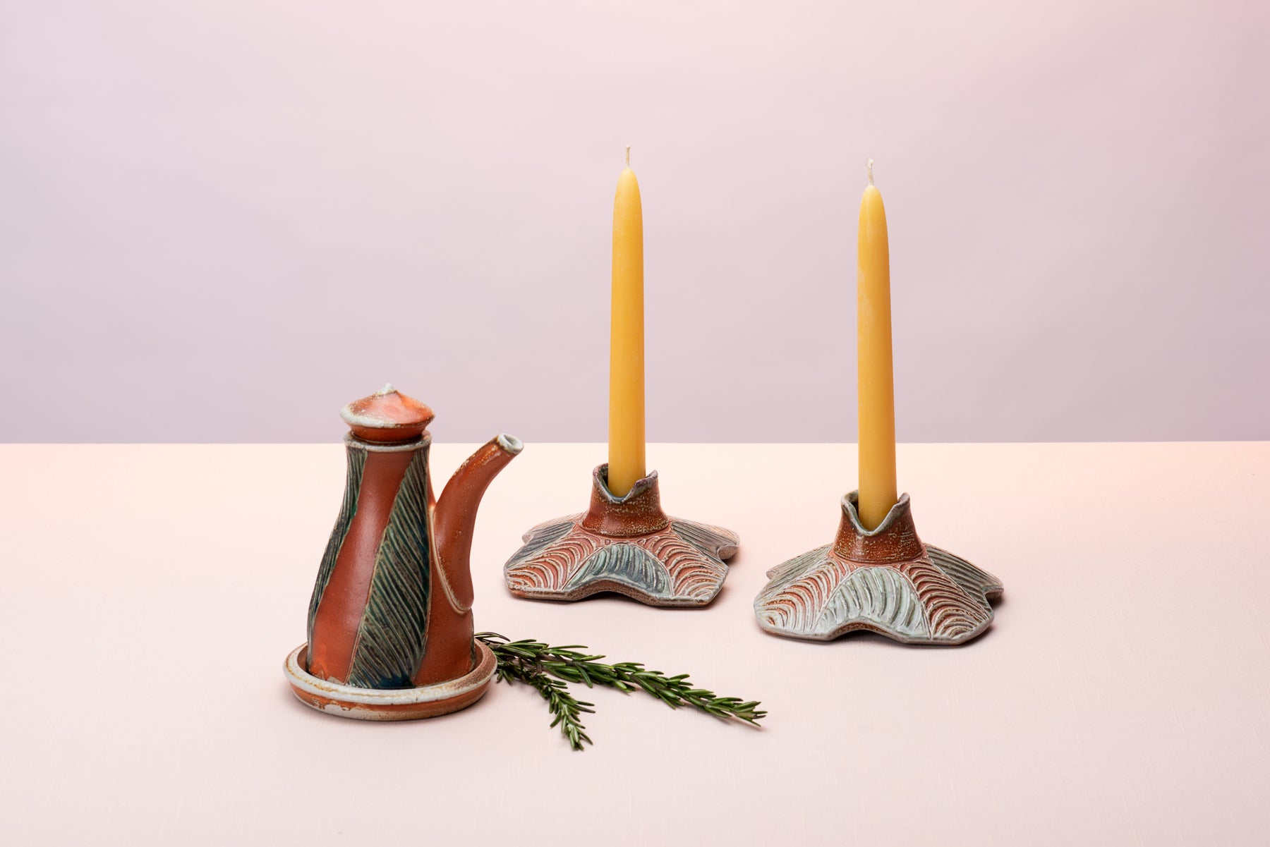 A handmade oil pourer and two handmade candlesticks by artist Joy Tanner sit on a peach table against a blushy backdrop. Image by Loam