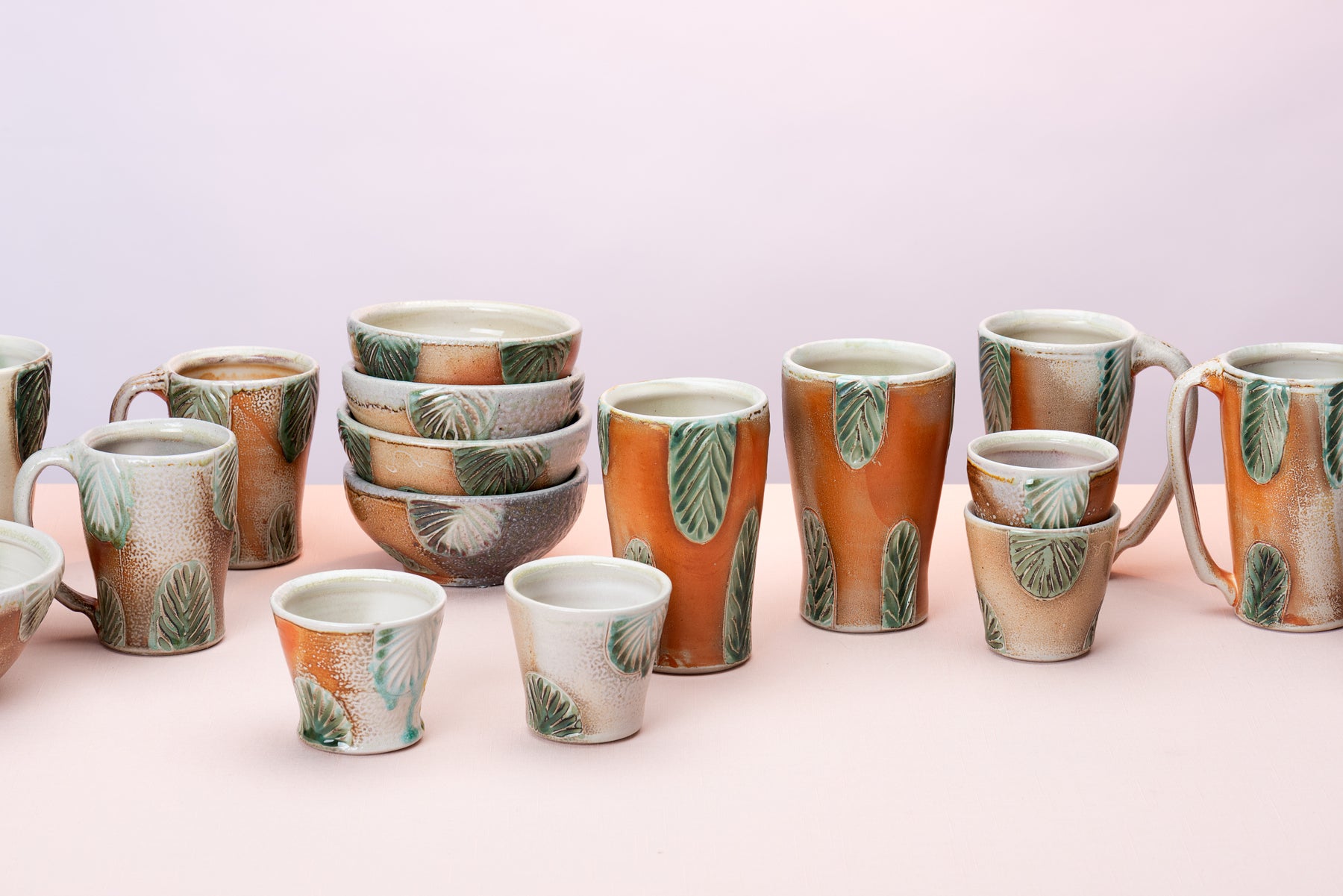 A group of handmade pots hand thrown and carved by artist Joy Tanner sit on a peach table against a blushy backdrop. Image by Loam