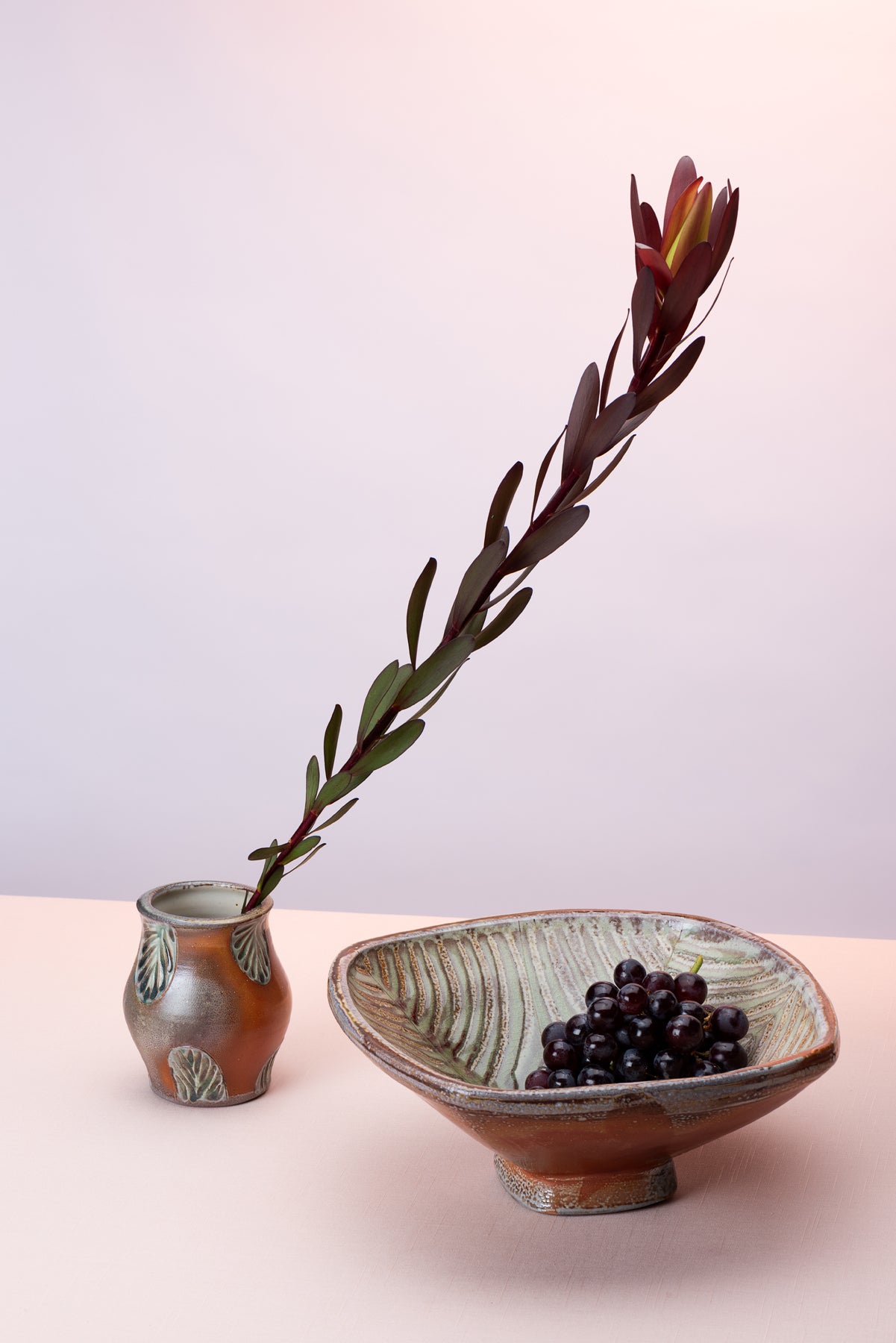 A couple pieces of handmade pottery by artist Joy Tanner sit on a peach table against a blush-purple  backdrop. Image by Loam 