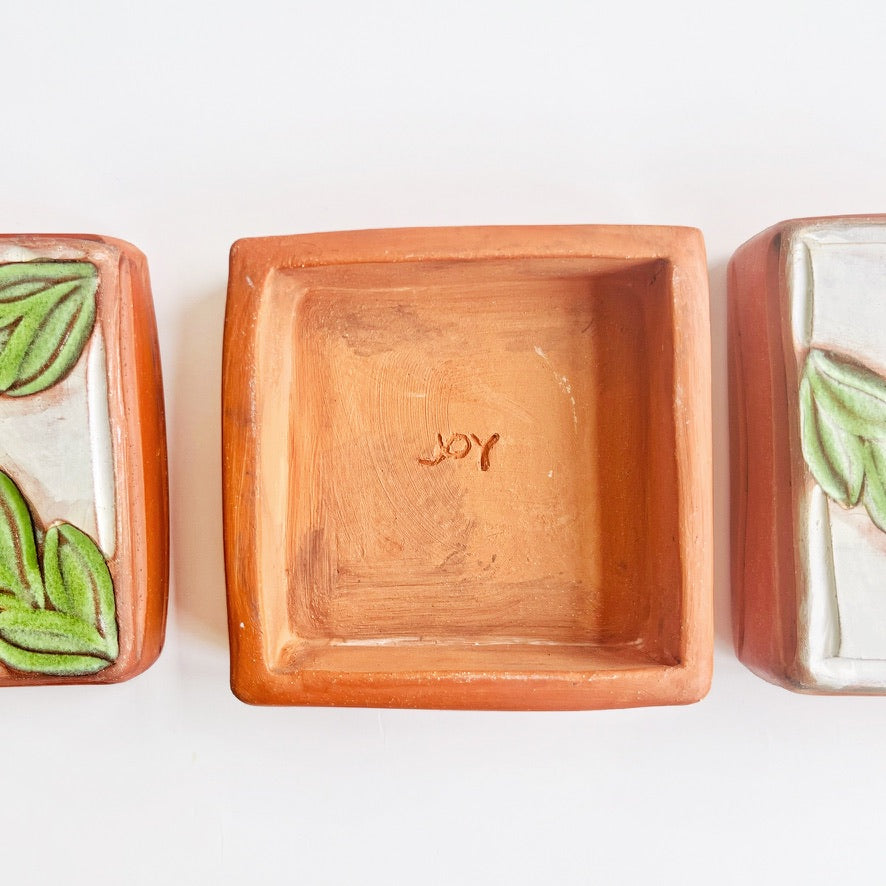 This square wall tile is made from red earthenware clay. The hand carved green leaf pattern contrasts nicely with the white surface and the red clay. Simply display on your wall alone, or in a grouping.