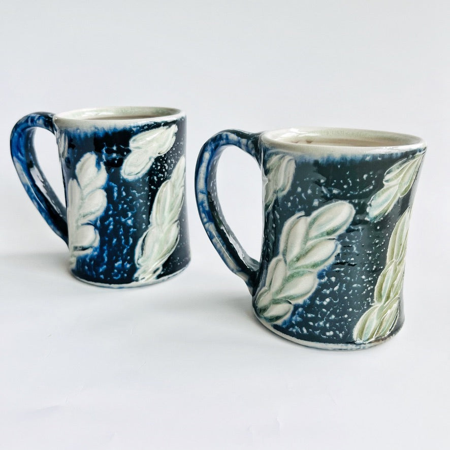 handmade black pottery mug with white and green leaf accents