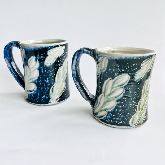 handmade black pottery mug with white and green leaf accents
