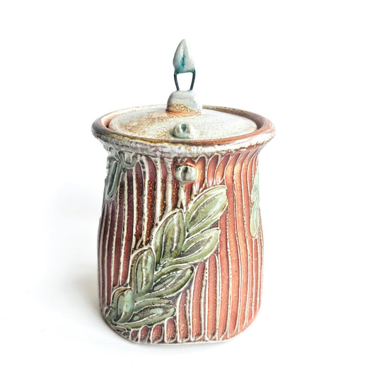 Ceramic jar with lid and leaf design on a white background