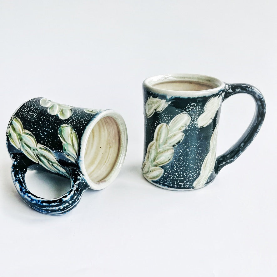 handmade black pottery mug with white and green leaf accents