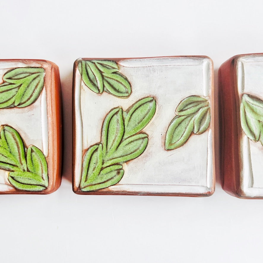 This square wall tile is made from red earthenware clay. The hand carved green leaf pattern contrasts nicely with the white surface and the red clay. Simply display on your wall alone, or in a grouping.