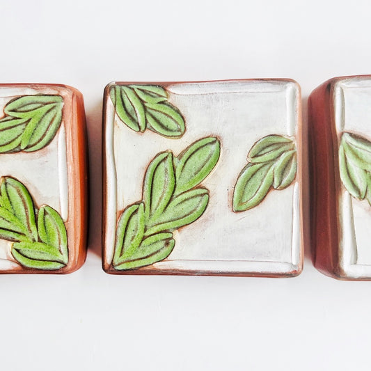This square wall tile is made from red earthenware clay. The hand carved green leaf pattern contrasts nicely with the white surface and the red clay. Simply display on your wall alone, or in a grouping.