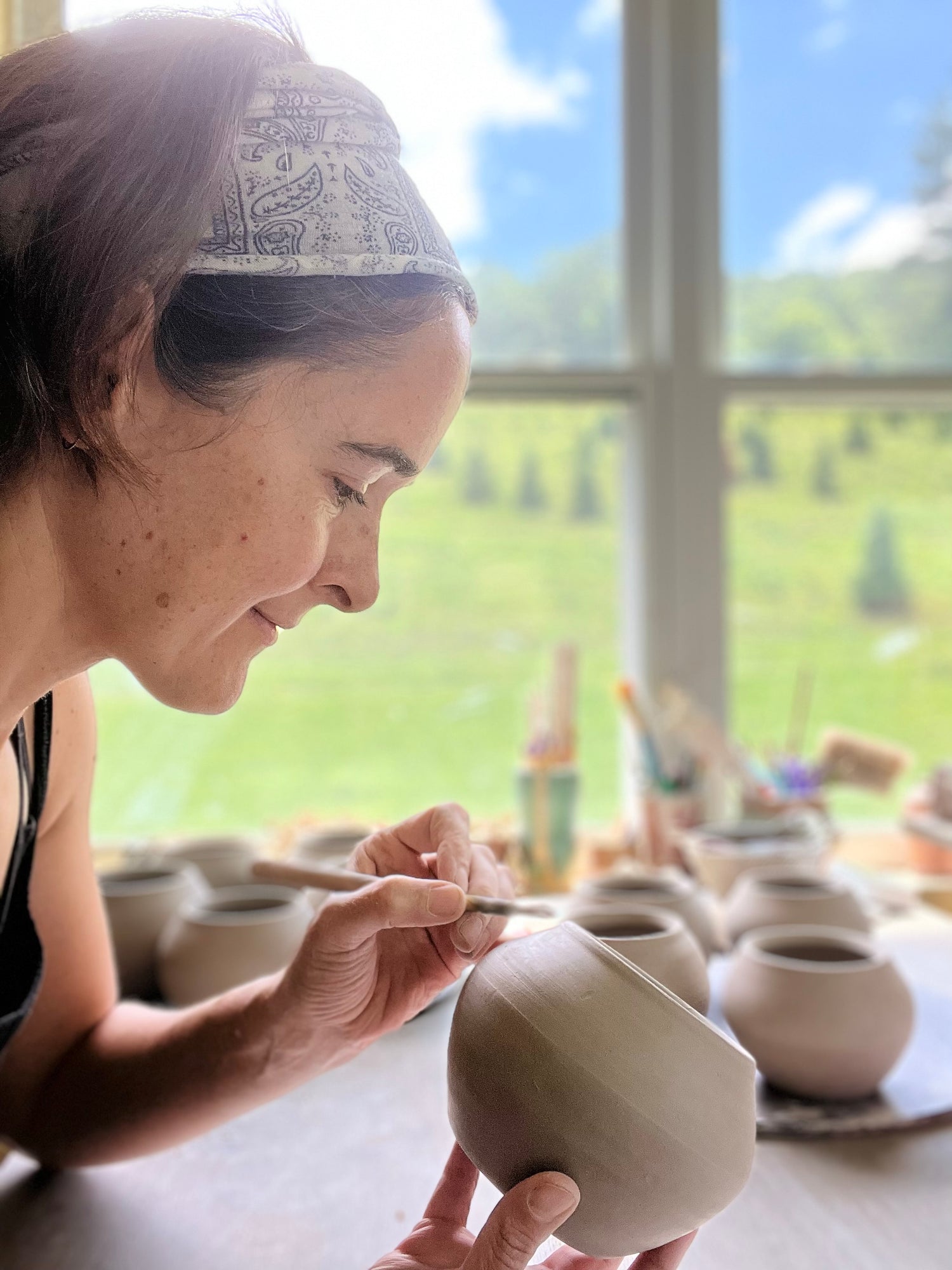 Joy Tannerworking with clay pottery in a bright room with large windows.