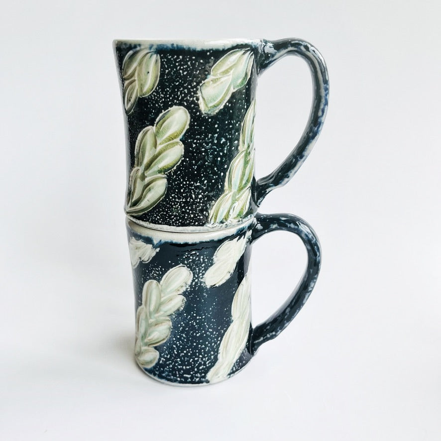 handmade black pottery mug with white and green leaf accents