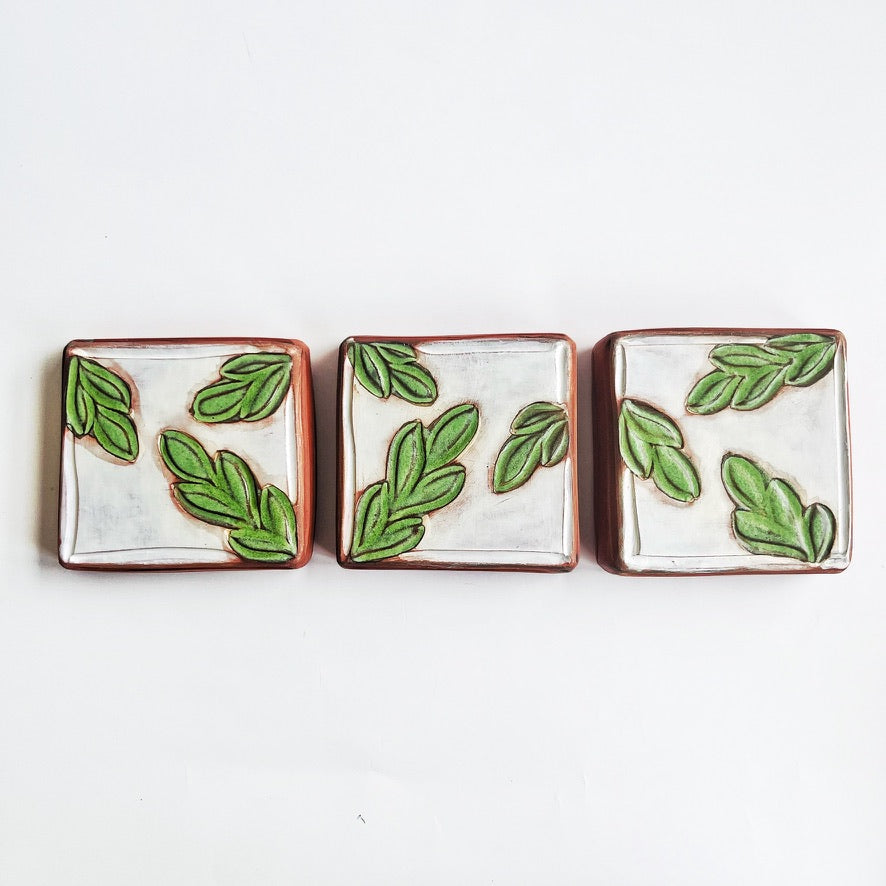 This square wall tile is made from red earthenware clay. The hand carved green leaf pattern contrasts nicely with the white surface and the red clay. Simply display on your wall alone, or in a grouping.