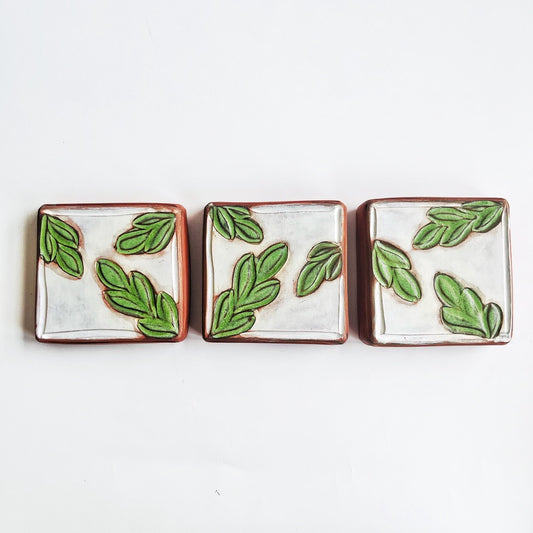 This square wall tile is made from red earthenware clay. The hand carved green leaf pattern contrasts nicely with the white surface and the red clay. Simply display on your wall alone, or in a grouping.