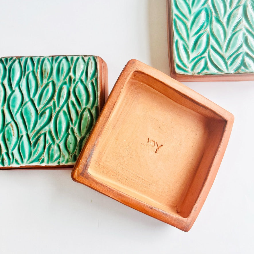 This square wall tile is made from red earthenware clay. The hand carved green leaf pattern contrasts nicely with the red clay. Simply display on your wall alone, or in a grouping.