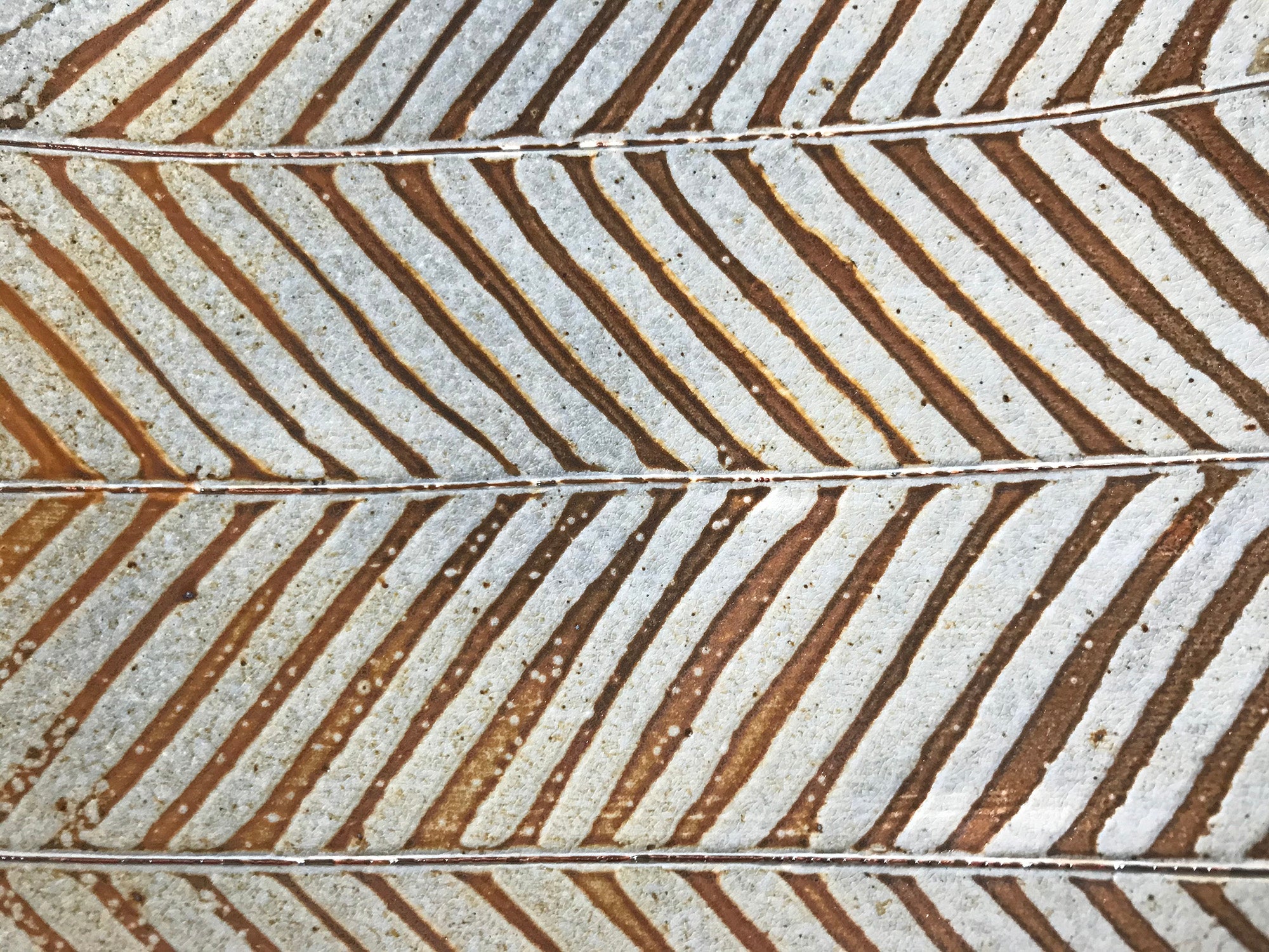 A detail of one of Joy Tanner's surface design patterns featuring brown and grey alternating diagonal lines of glaze. 