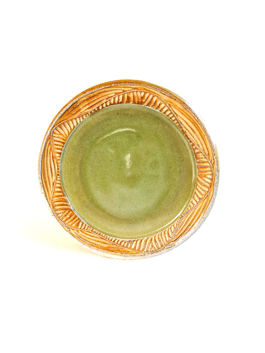 A handmade plate makes your food taste better. This plate is wheel thrown from stoneware clay. The leaf pattern that is hand carved is inspired by nature. The rim is yellow and the interior of the plate is light green.