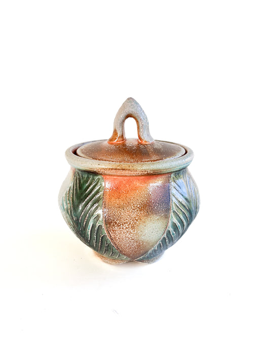 This small round handmade jar could be used to store tea bags, sugar, or candy. The green leaf pattern that is hand carved is inspired by nature. 