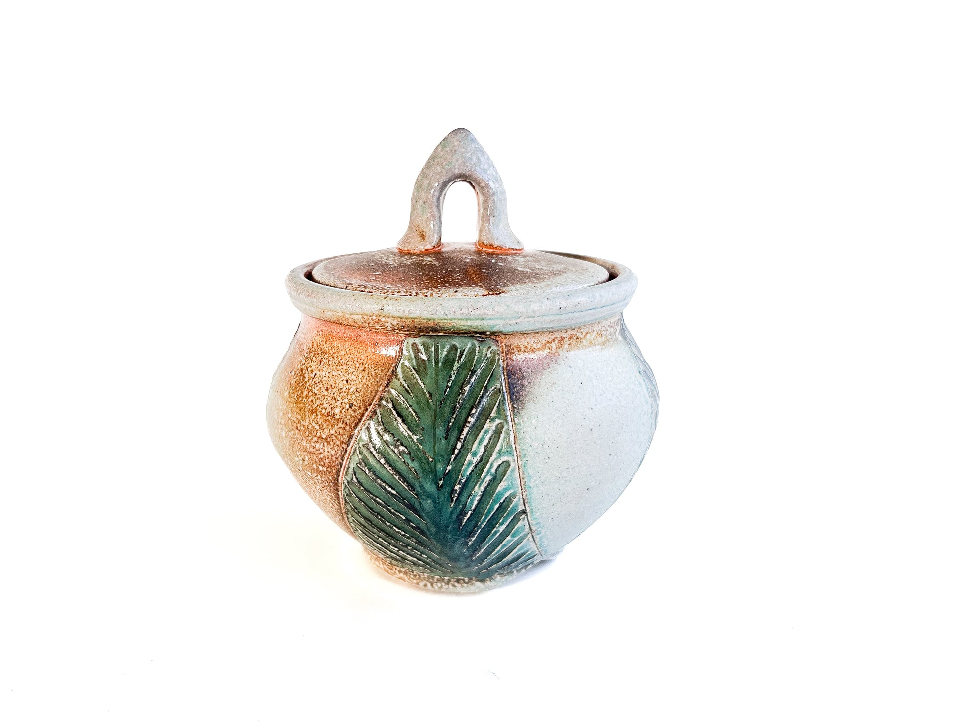 This small round handmade jar could be used to store tea bags, sugar, or candy. The green leaf pattern that is hand carved is inspired by nature. 