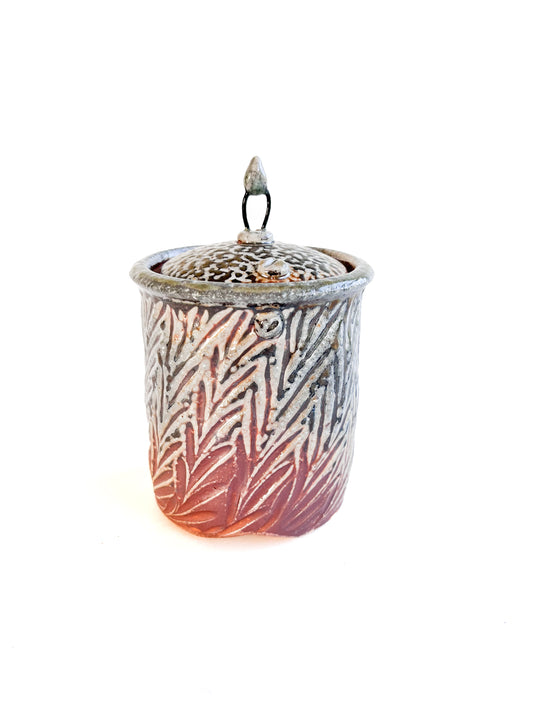 This small square handmade jar could be used to store tea bags, sugar, or candy. The leaf pattern that is hand carved is inspired by nature. There is a wire and clay knob on top of the lid.