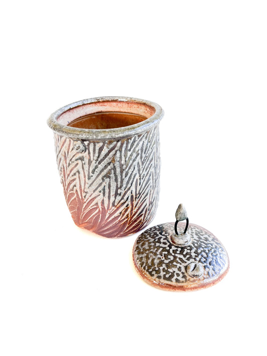 This small square handmade jar could be used to store tea bags, sugar, or candy. The leaf pattern that is hand carved is inspired by nature. There is a wire and clay knob on top of the lid.