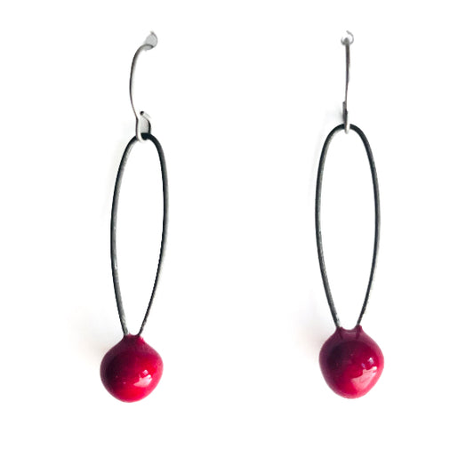 Pair of earrings with red spherical beads on black strings against a white background