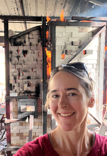 Joy Tanner in front of her soda kiln that is hot with flames.