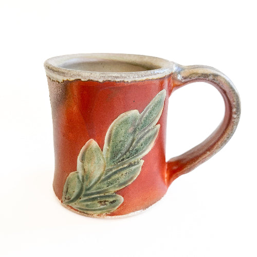 Red ceramic mug with green leaf design on a white background